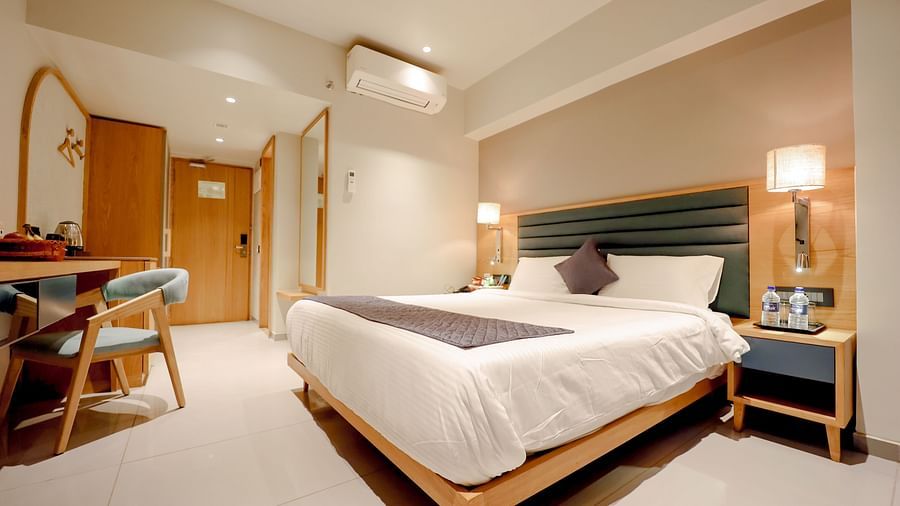 An image of a bedroom with double size bed, bedside table with lamp and other furniture - Pride Resort Ambaji